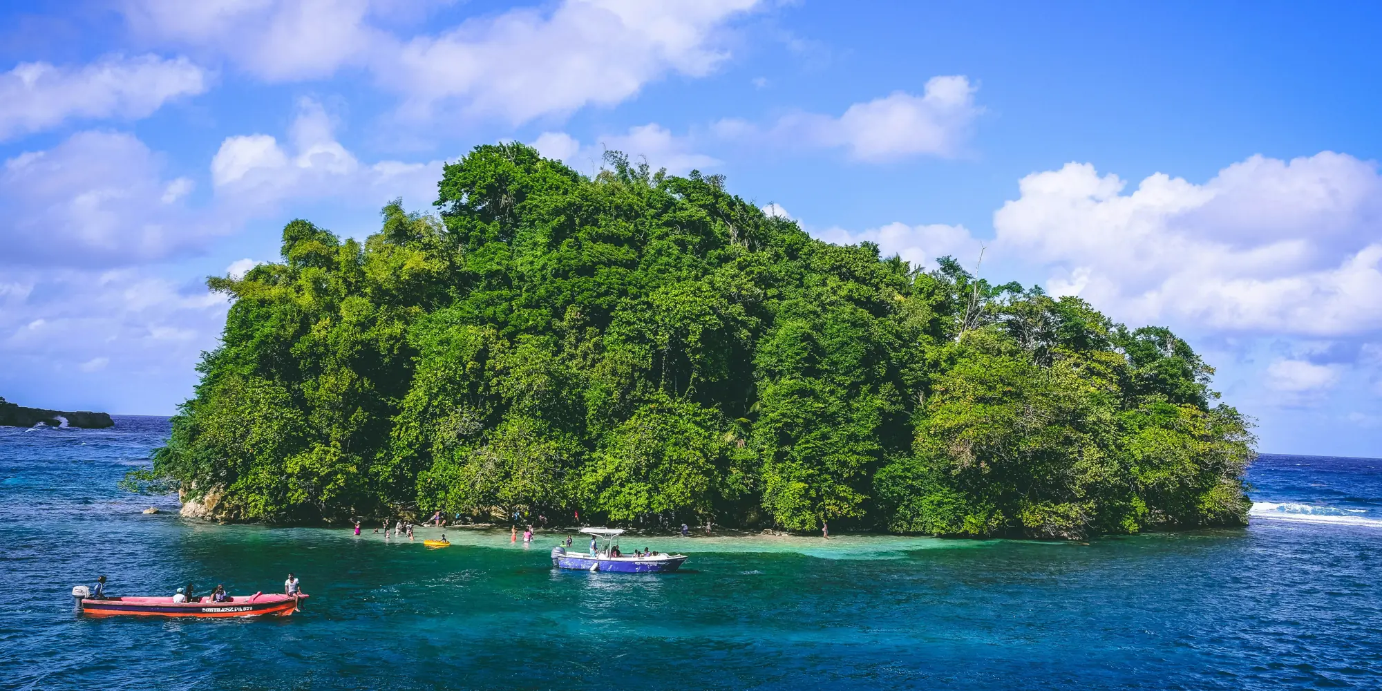 Piccola isola verde con barche nel mare davanti alla Giamaica, immersioni con squali