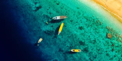 Veduta aerea di barche in acque costiere turchesi accanto a una spiaggia sabbiosa