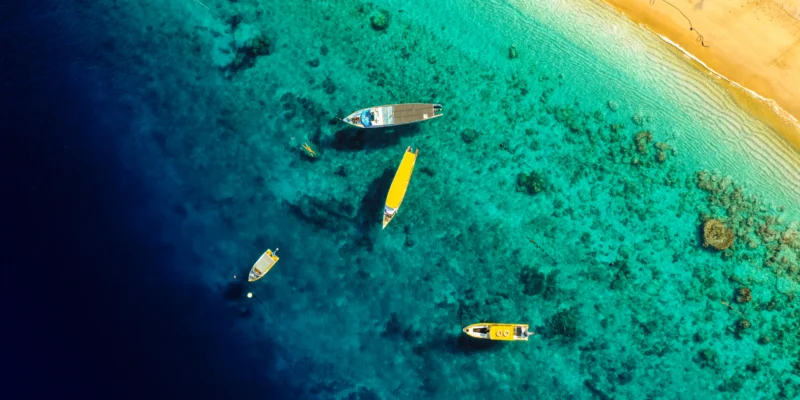 Veduta aerea di barche in acque costiere turchesi accanto a una spiaggia sabbiosa