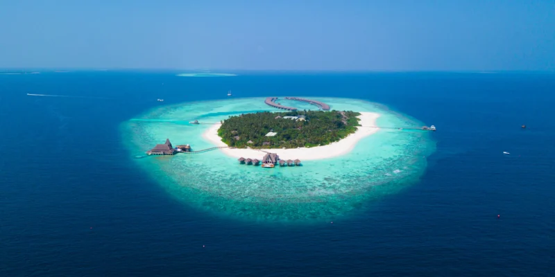 Vista aerea di un’isola alberata con spiaggia bianca e laguna turchese alle Maldive