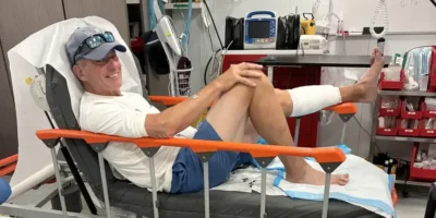 John Schweizer seduto su un letto d'ospedale dopo il morso di squalo alle Bahamas, con la parte inferiore della gamba sinistra fasciata