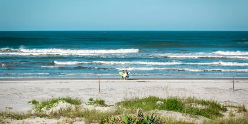 Due persone con tavole da surf sulla spiaggia di New Smyrna Beach, con le onde sullo sfondo